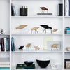Wooden bird figurines in natural tones, black accents, and minimalist design on a white shelf. Elegant decor arrangement.