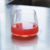 Clear glass tumbler with a smooth, modern shape, filled with a vibrant pink drink against a polished metal surface.