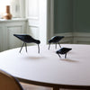 Three black bird sculptures on a round pink table, highlighting sleek shapes and minimalist design.