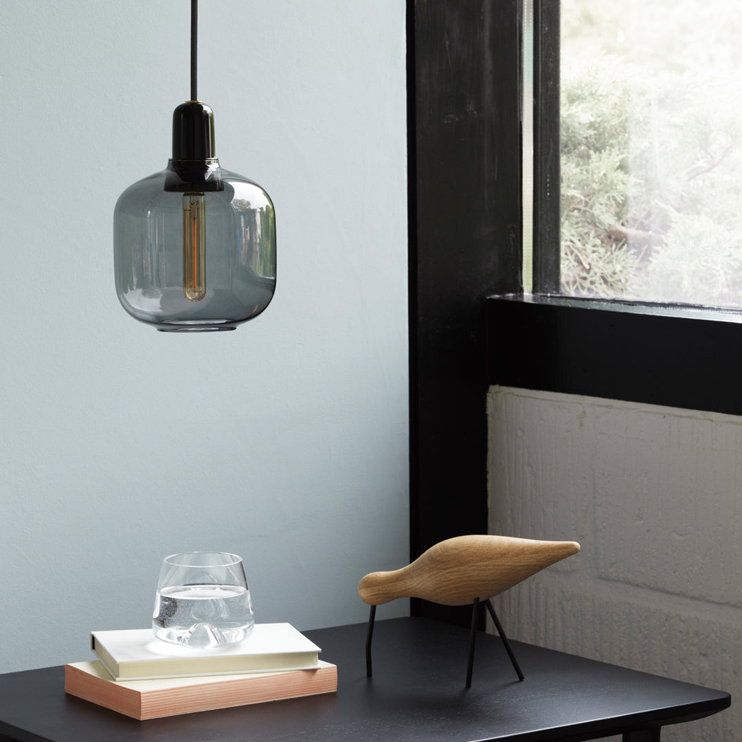 "Stylish glass pendant light with a smoky gray finish, juxtaposed against a minimalist black and pastel tabletop."