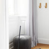 Gray velvet pouf, light gray curtains, natural wood hooks, and warm brown flooring in a bright interior.