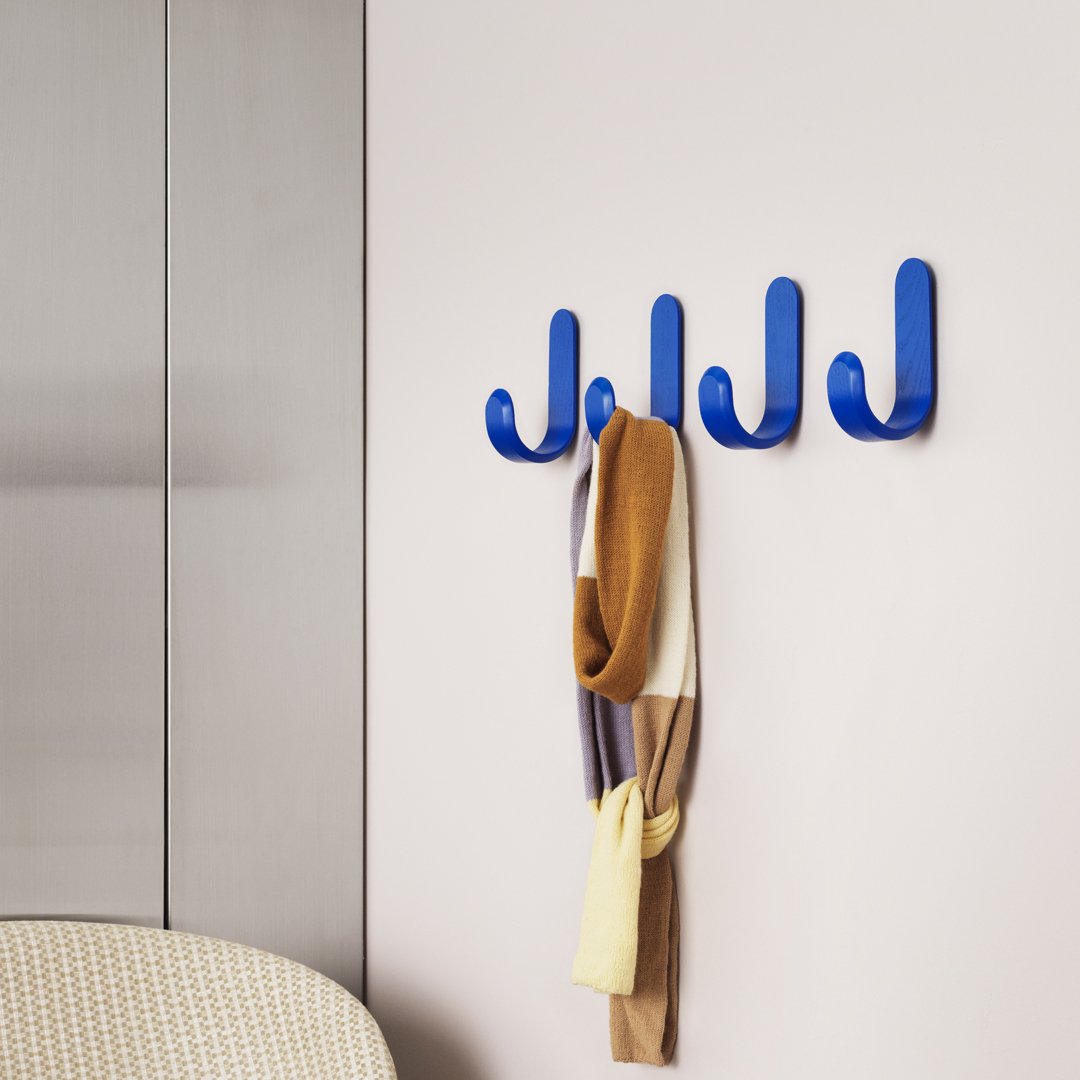 Bright blue wall hooks displaying a cozy scarf in earthy tones, enhancing modern decor with playful patterns.