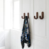 Black and blue floral-patterned scarf hanging on brown hooks against a white wall backdrop.