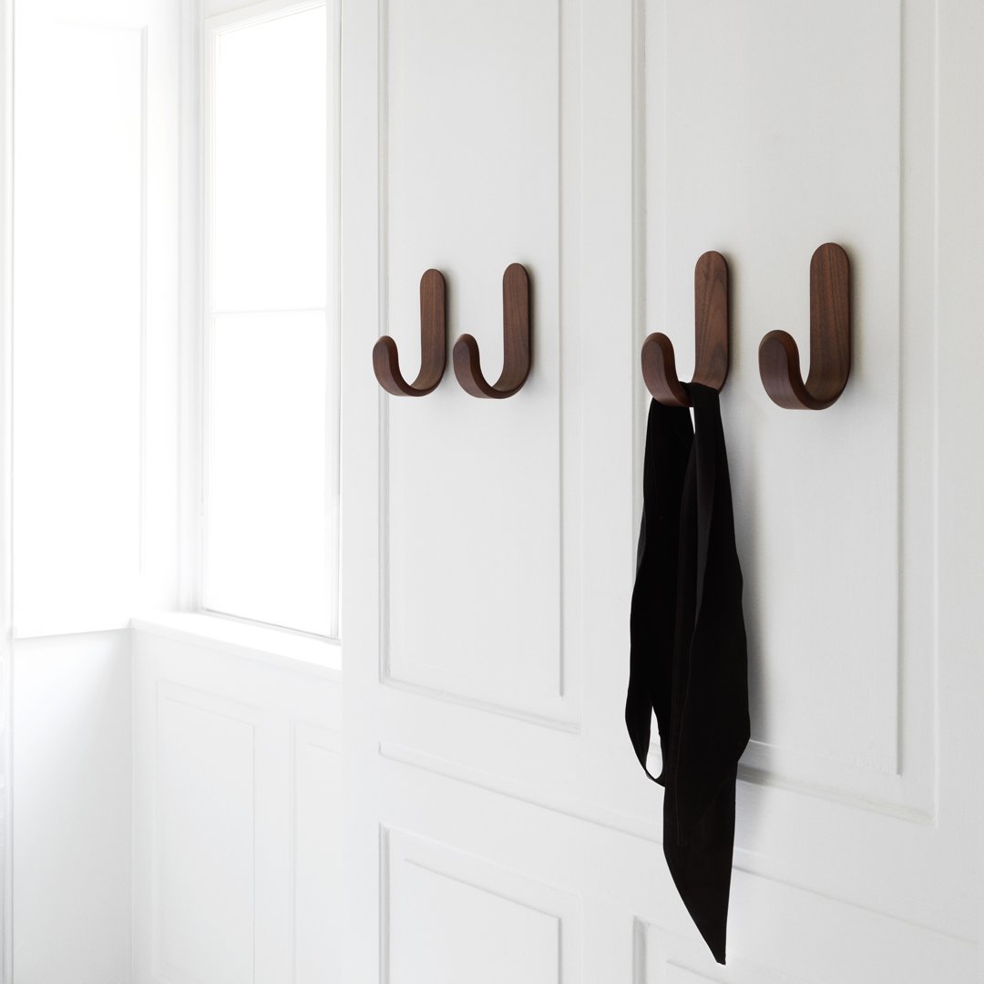 Brown wall hooks on white paneling, showcasing a minimalist design with a black tie hanging.