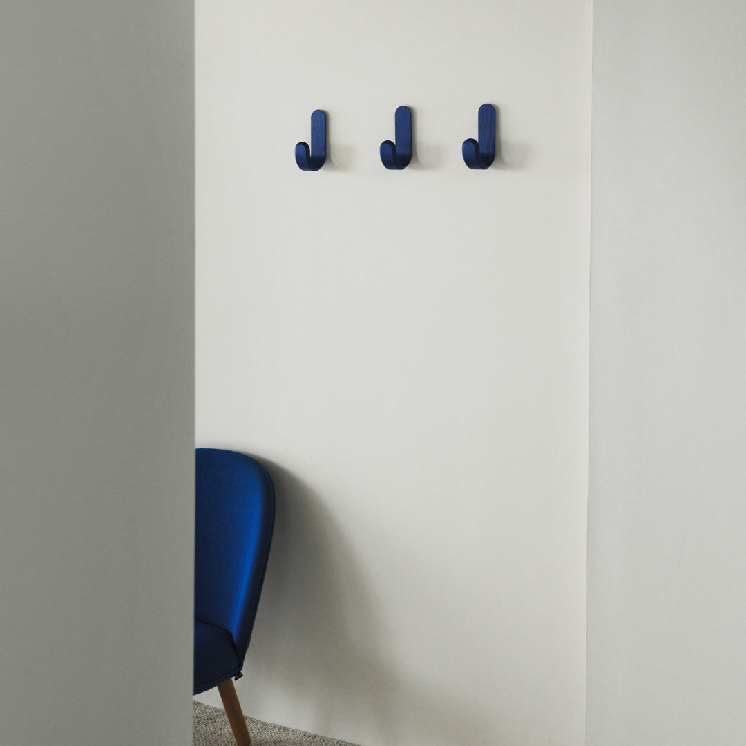 Three navy blue wall hooks against a minimalist white wall, complemented by a sleek blue chair.