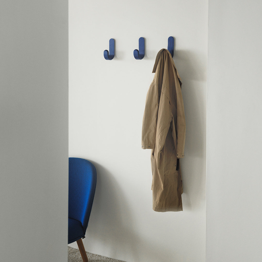 Navy blue coat hooks against a neutral wall, with a brown coat draped, complemented by a vibrant blue chair.