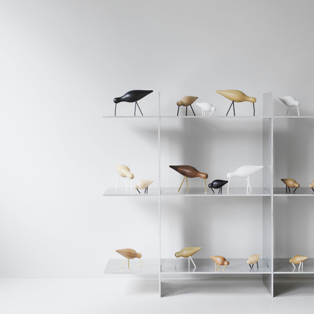 Assorted decorative bird figurines in black, white, and natural wood tones on a modern displayed shelf.