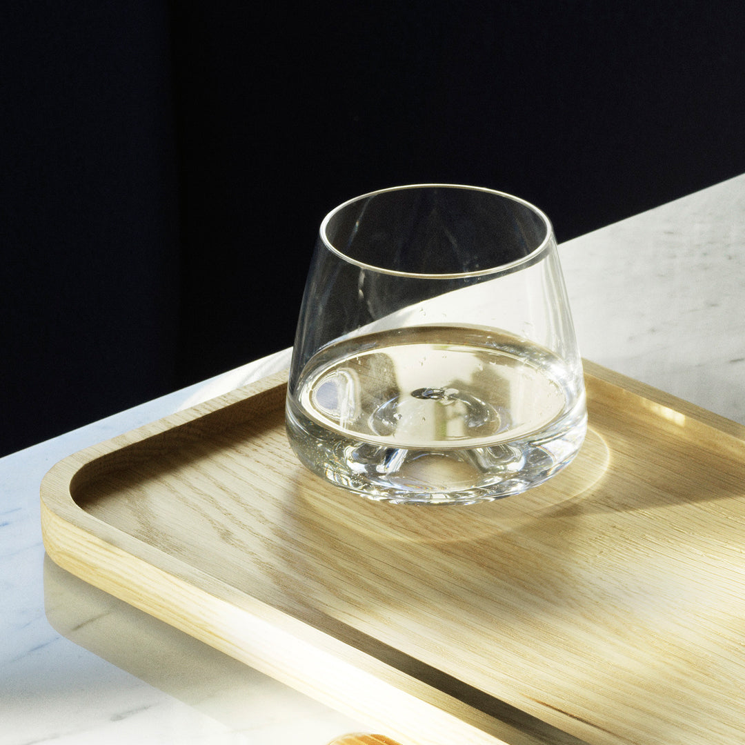 Clear glass tumbler on a natural wood tray, contrasting against dark background. Elegant and minimalist design.