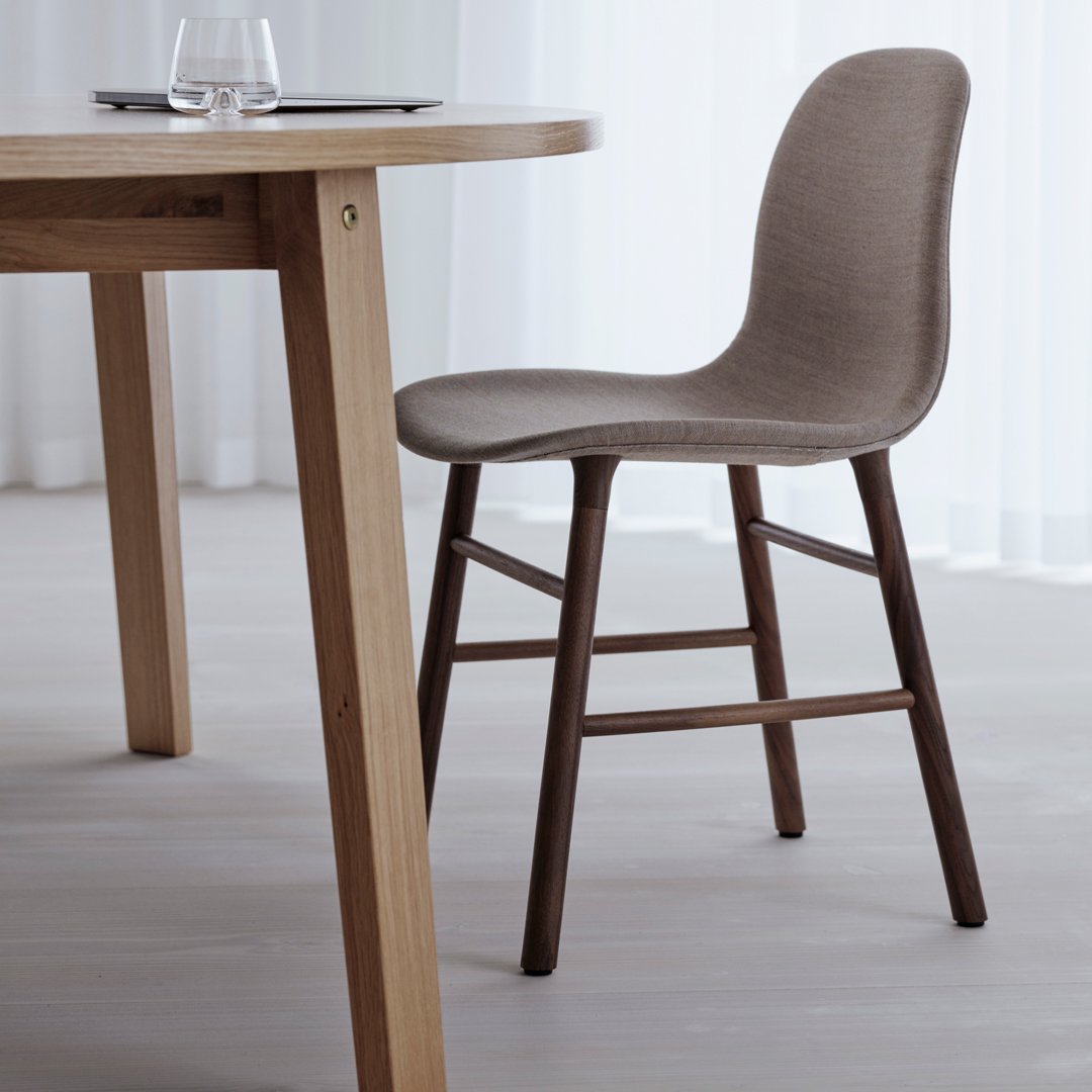 Neutral beige fabric upholstery on a sleek, modern chair with dark wooden legs against a light, airy background.