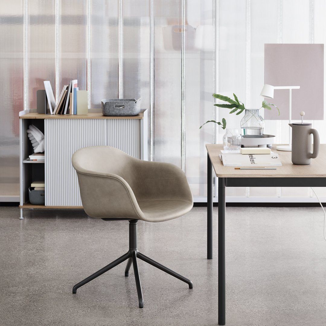 Stylish taupe chair with soft curves, set against a light wood desk and neutral decor elements in a modern space.