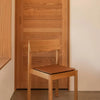 Wooden chair with a natural finish and a warm brown leather seat, set against a neutral beige background.