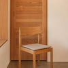Natural wood chair with a smooth finish and a light gray cushion against a warm wood backdrop. Simple and modern design.
