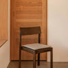 Dark wood chair with light gray cushion against a warm wooden background. Minimalist design with natural tones.
