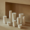 Assorted white ceramic vases with various geometric shapes against a neutral beige backdrop.