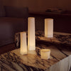Elegant white candle holders with soft, warm glow on a marbled stone table. Minimalist design enhances cozy ambiance.