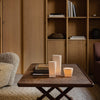 Wooden table with earthy tones, neutral candles, and soft textures in a cozy, minimalistic living space.
