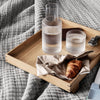 Clear textured glassware on a natural wood tray, accompanied by a beige napkin and a golden croissant on a gray patterned blanket.