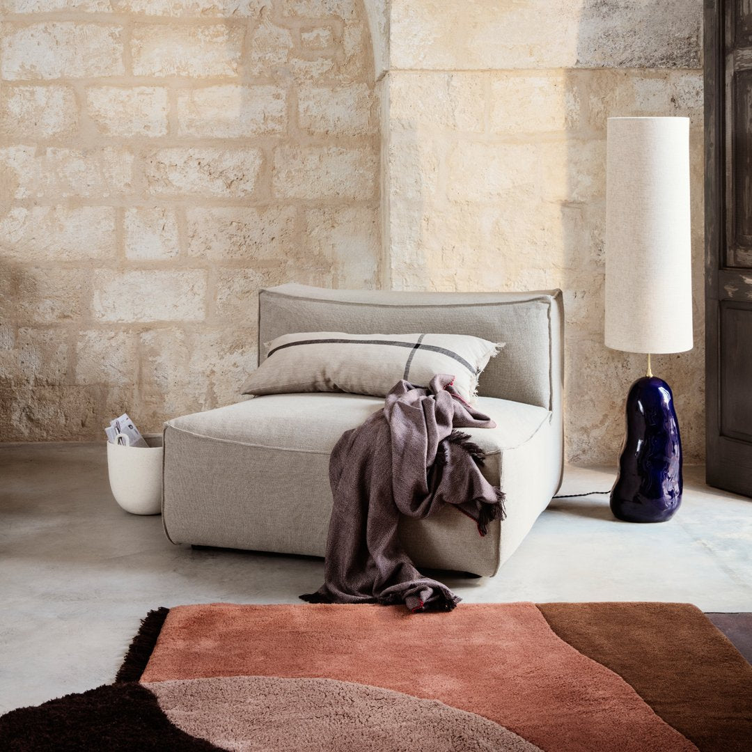 Gray modular chair with textured fabric, accented by a soft purple throw and a colorful abstract rug in earthy tones.