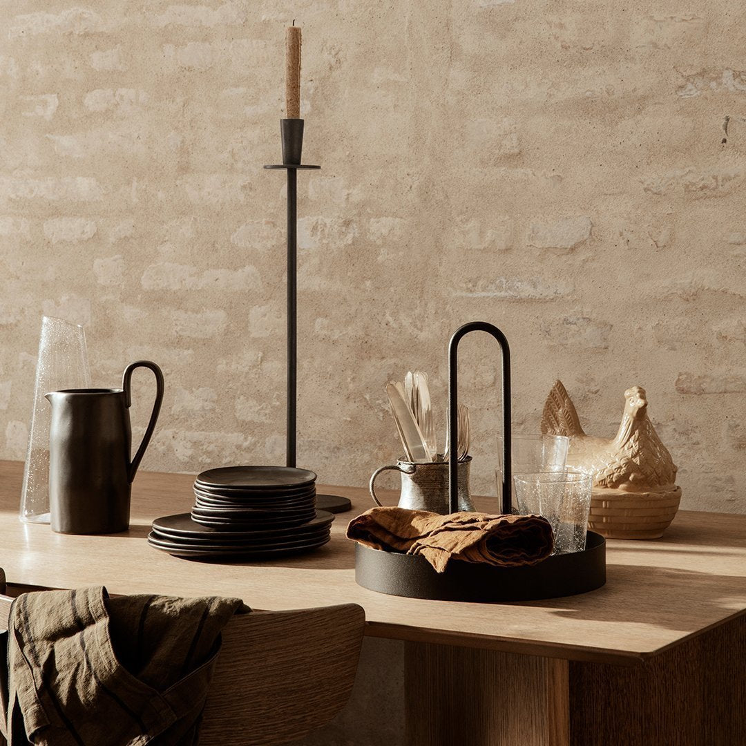 Elegant rustic dining setup with black plates, natural wood tones, and earthy textures against a neutral background.