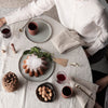 "Neutral table setting with earthy tones, textured napkins, and decorative patterns, featuring a circular cake centerpiece."