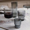Set of smoky gray glass tumblers with vertical ribbed patterns on a textured tablecloth.