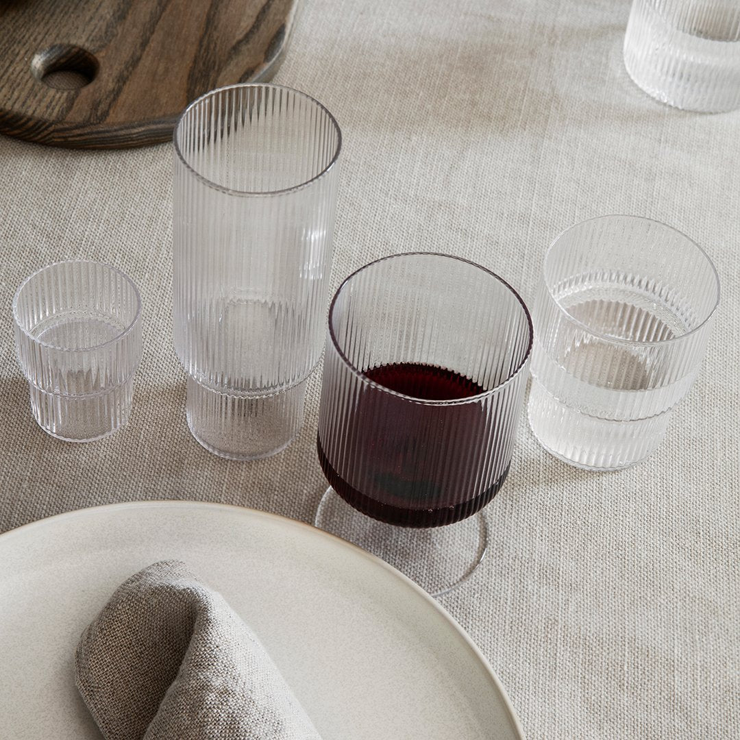 "Set of ribbed glassware in clear, smoke gray, and deep wine hues on a neutral table setting."