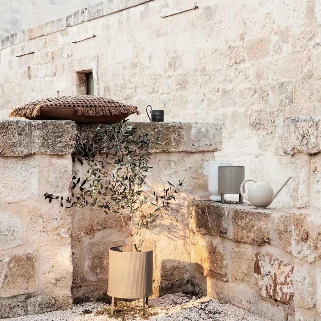 Neutral tones with textured patterns on a decorative pillow and minimalist planters set against a rustic stone backdrop.