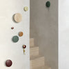 Colorful round wall hooks in shades of green, brown, yellow, and natural wood against a minimalist beige background.
