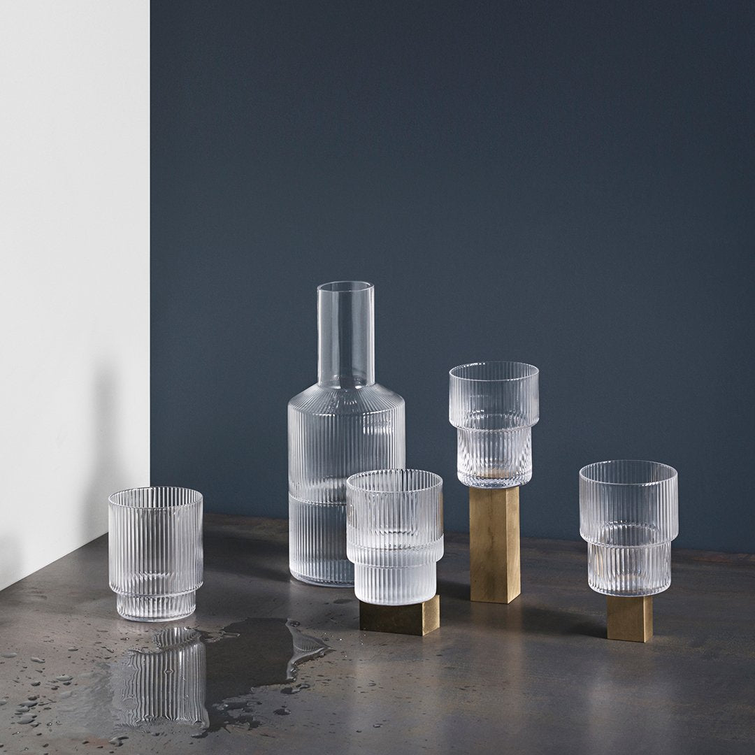 Frosted glass drinkware set with clear and gold accents against a dark gray background. Modern, minimalist design.