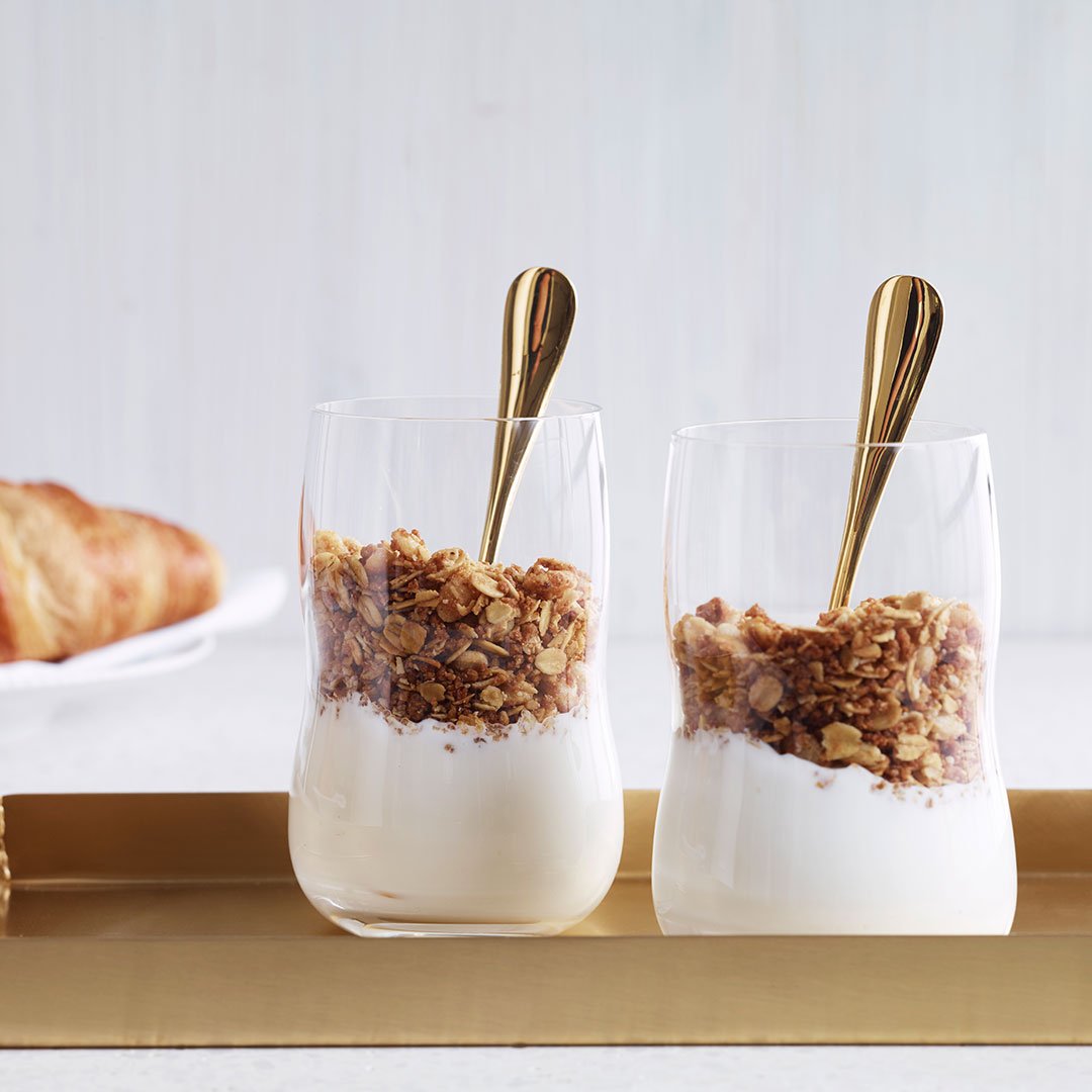 Two clear glass cups filled with layered yogurt and granola, featuring a creamy white and brown color scheme.