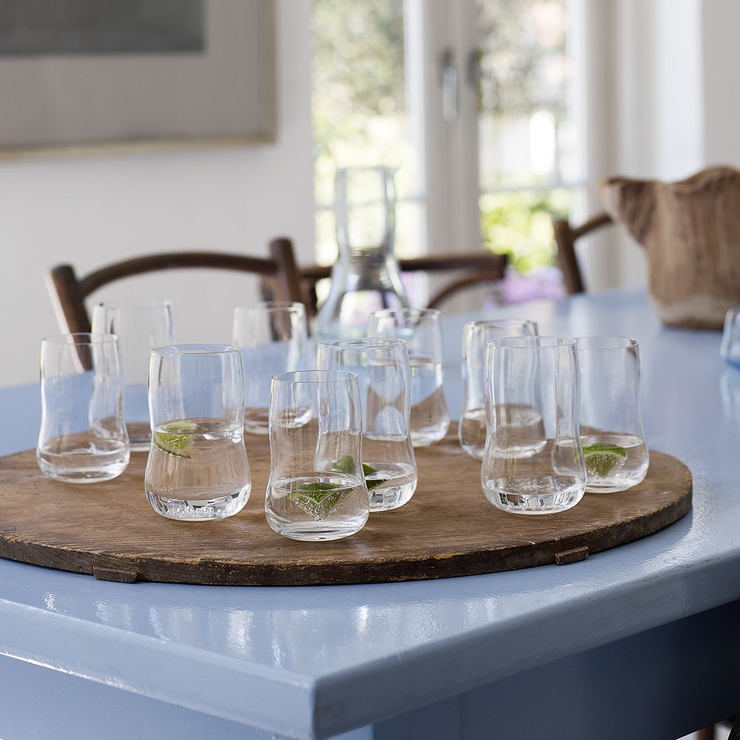 Set of clear glass tumblers on a round wooden tray, featuring fresh lime slices, against a light blue table.