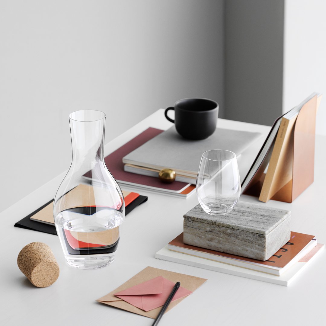 Clear glass carafe and tumbler on a minimalistic desk with black, white, and earthy tones, featuring geometric patterns.