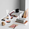 Clear glass carafe and tumbler on a minimalistic desk with black, white, and earthy tones, featuring geometric patterns.