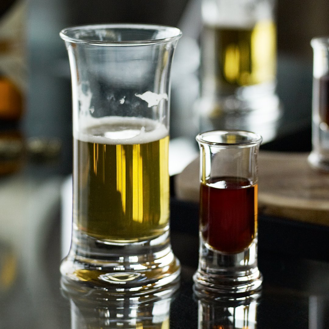 "Clear glass shot and beer glasses showcasing golden and deep amber liquids reflecting light."