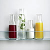 Four stylish glass bottles displaying vibrant hues: deep red, clear with green mint, creamy white, and bright yellow.