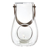 Clear glass lantern with a circular cutout, accented by a brown leather handle and a subtle candle glow.