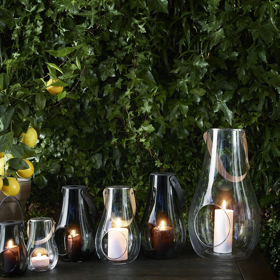 Elegant glass candle holders in clear and black, featuring smooth curves and glowing candles against a lush green backdrop.