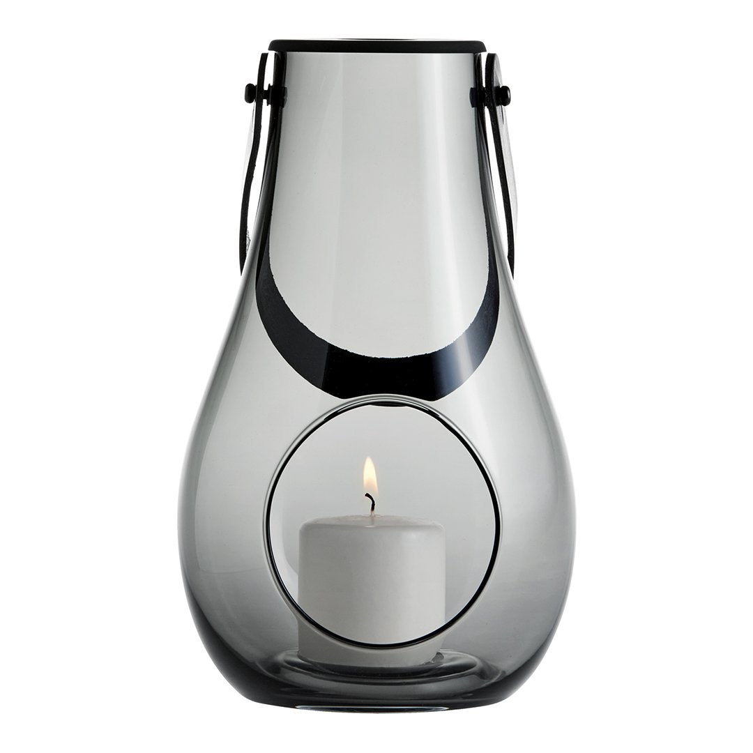 Clear glass lantern with elegant black accents and a circular opening, showcasing a white candle inside.