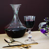 Elegant wine decanter and vintage glass, showcasing deep red hues against a dark backdrop. Gold-tinted cutlery accents.