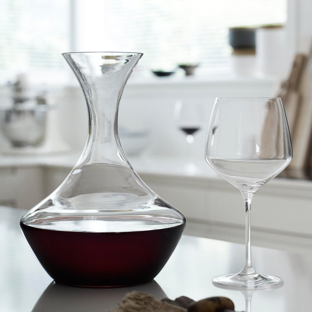 Clear glass decanter with a dark red base, paired with a transparent wine glass, accentuating elegant simplicity.