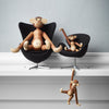 Wooden monkey figurines in natural tones on modern black chairs against a light gray wall, showcasing playful designs.