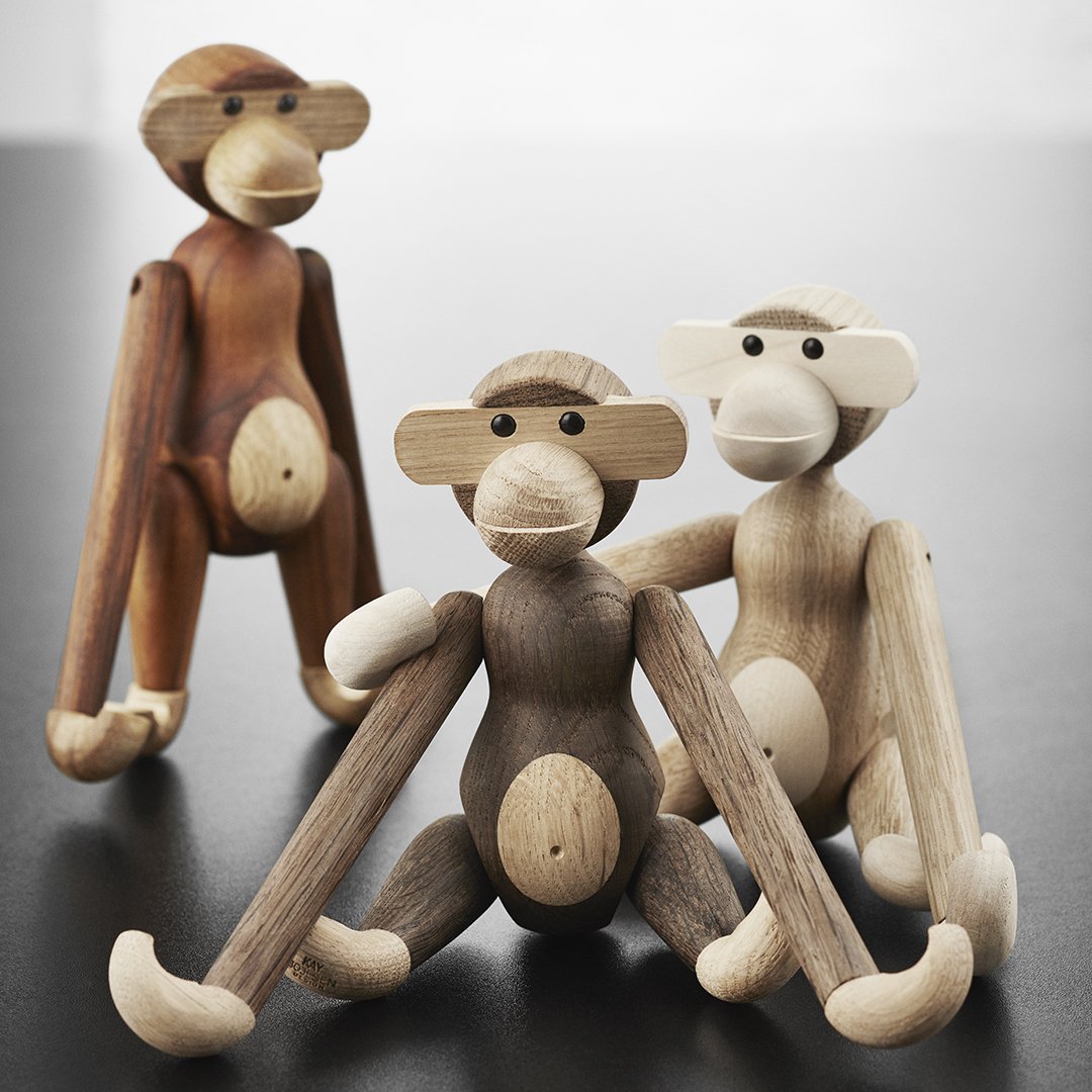 "Three wooden monkey figurines in shades of brown, tan, and cream with natural wood grain patterns and playful designs."