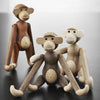 "Three wooden monkey figurines in shades of brown, tan, and cream with natural wood grain patterns and playful designs."