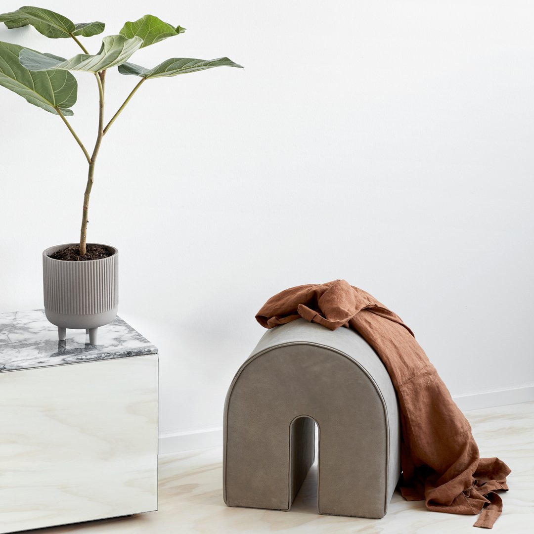 Gray arch-shaped stool, terracotta blanket draped, marble tabletop, potted plant, minimalist decor.
