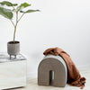 Gray arch-shaped stool, terracotta blanket draped, marble tabletop, potted plant, minimalist decor.