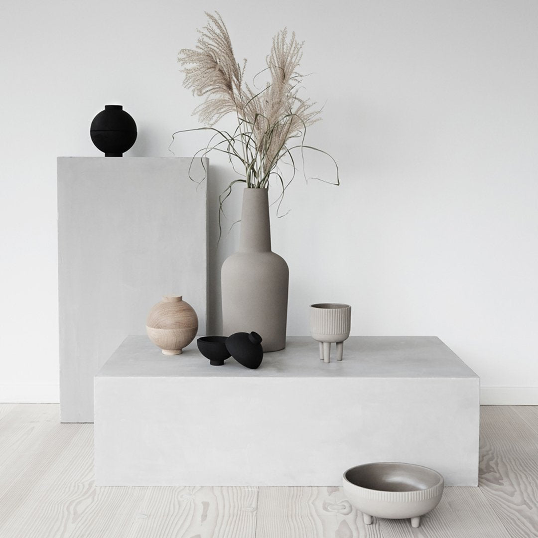 Gray and beige decor with organic shapes and textures, featuring a black vase and a light brown bowl. Elegant minimalism.
