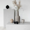 "Neutral-toned vases and decor with textures, featuring black, grey, and earthy shades on minimalist surfaces."