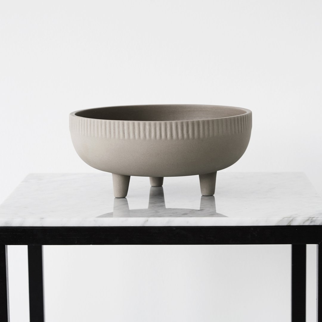 Gray ceramic bowl with textured ribbed pattern, featuring three short legs, displayed on a marble surface.