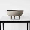 Gray ceramic bowl with textured ribbed pattern, featuring three short legs, displayed on a marble surface.