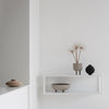 Neutral tones with soft beige and black accents; minimalist decor on a white shelf against a light background.